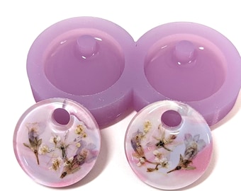 May include: A light purple silicone mold with two circular cavities, each with a small hole. Two clear, round resin pendants with dried flowers are next to the mold. The pendants have a hole at the top for hanging.
