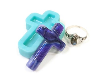 May include: A blue silicone mold shaped like a cross, with a purple and blue resin cross inside. A silver ring with a dark blue stone is also in the image.