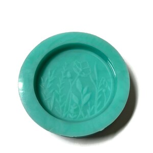 Pode incluir: Uma forma de silicone verde-azulada com um desenho em relevo de flores e folhas estilizadas.