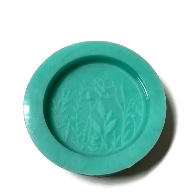 Pode incluir: Uma forma de silicone verde-azulada com um desenho em relevo de flores e folhas estilizadas.