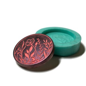 Pode incluir: Uma forma de silicone redonda com um design floral. A forma &eacute; verde-azulada e o design &eacute; marrom escuro com detalhes florais vermelhos.