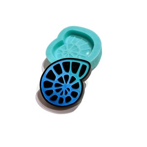 May include: A blue and green gradient resin cast of a nautilus shell with a black outline. The resin cast is sitting next to a teal silicone mold of the same shell.