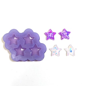 May include: A lilac silicone mould with star-shaped cavities, next to finished star-shaped resin pieces. The resin stars are decorated with glitter in shades of purple and white, creating a sparkling effect. The items are on a white background.