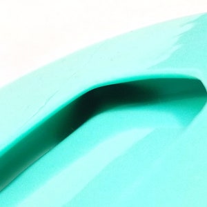 May include: A close-up of a turquoise plastic container with a handle. The container is smooth and shiny.