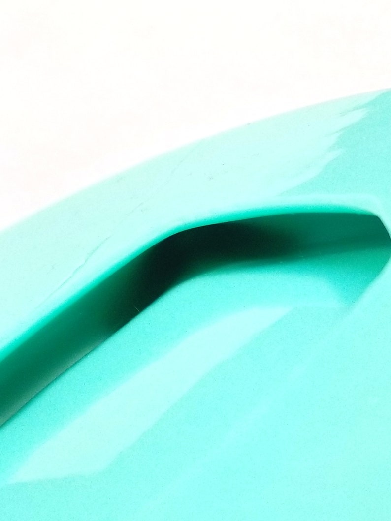 May include: A close-up of a turquoise plastic container with a handle. The container is smooth and shiny.