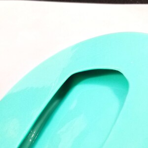 May include: A turquoise blue silicone soap dish with a cutout handle. The dish is designed to hold a bar of soap and drain excess water.