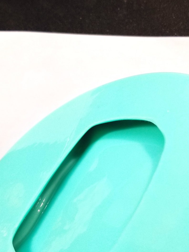 May include: A turquoise blue silicone soap dish with a cutout handle. The dish is designed to hold a bar of soap and drain excess water.