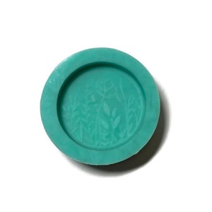 Pode incluir: Um molde de silicone turquesa com um design em relevo de um arranjo floral. O molde &eacute; redondo e tem uma superf&iacute;cie lisa.