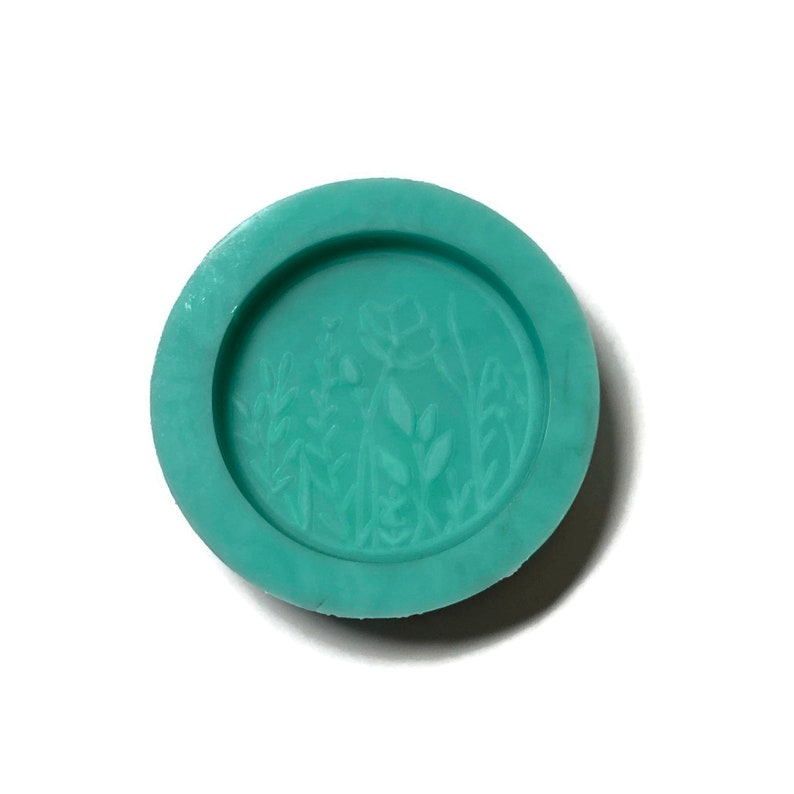 Pode incluir: Um molde de silicone turquesa com um design em relevo de um arranjo floral. O molde &eacute; redondo e tem uma superf&iacute;cie lisa.