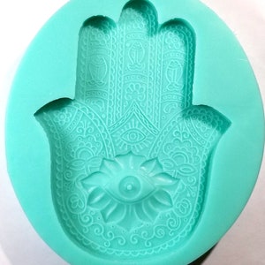 May include: A turquoise silicone mold shaped like a hamsa hand with intricate details and an eye in the center.