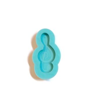 Puede incluir: Un molde de silicona azul claro con forma de clave de sol. El molde está diseñado para hacer dijes de resina o arcilla polimérica.