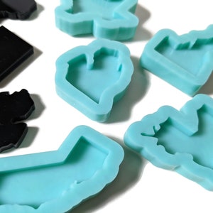 May include: A set of silicone molds for making resin crafts. The molds are shaped like different states in the United States, including California, New York, and Texas. The molds are light blue and have a smooth, glossy finish.