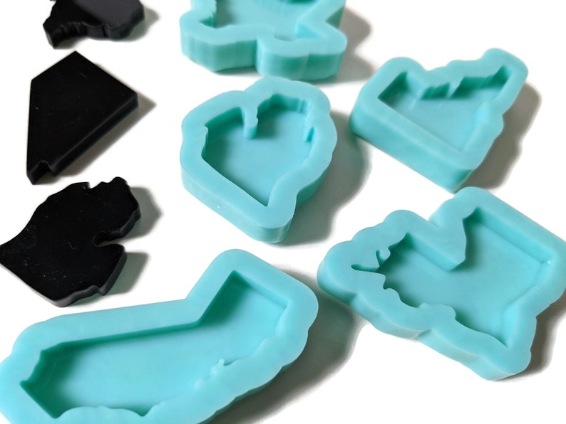 May include: A set of silicone molds for making resin crafts. The molds are shaped like different states in the United States, including California, New York, and Texas. The molds are light blue and have a smooth, glossy finish.