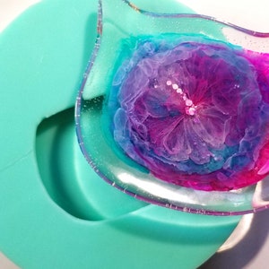 May include: A clear resin tray with a pink, purple, and blue abstract floral design. The tray is sitting in a teal silicone mold.