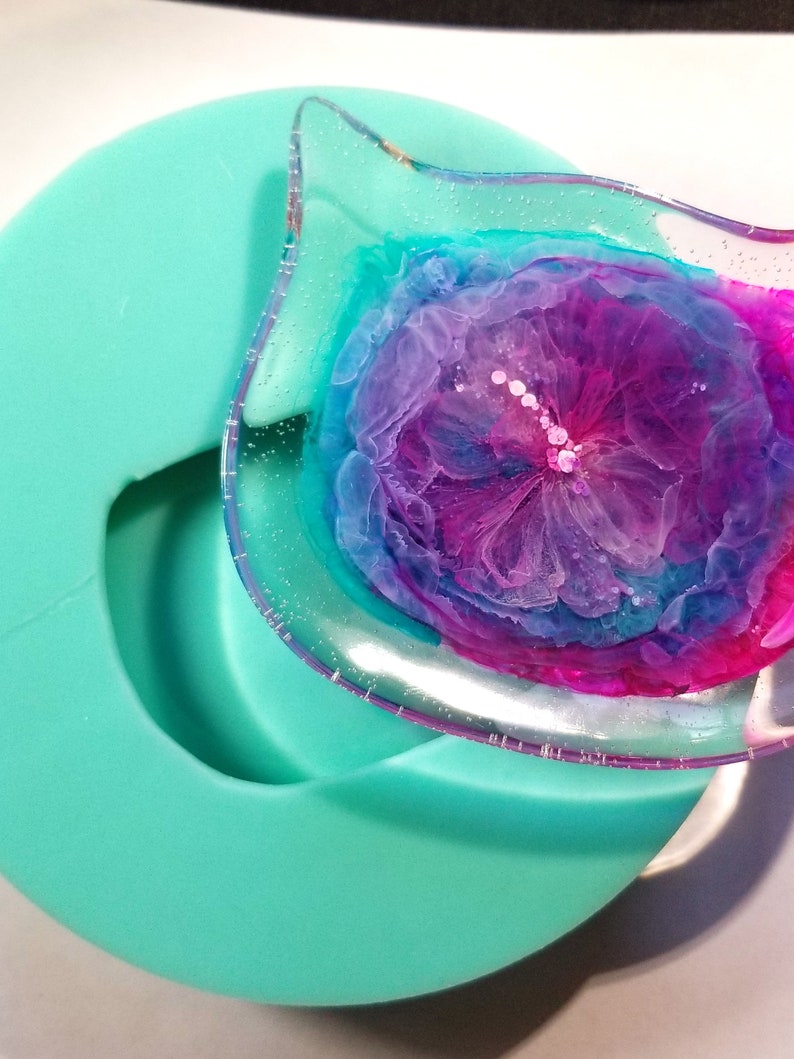 May include: A clear resin tray with a pink, purple, and blue abstract floral design. The tray is sitting in a teal silicone mold.