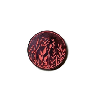 Pode incluir: Um descanso de copo circular de cor vermelho escuro com um desenho de flores e folhas cor-de-rosa.