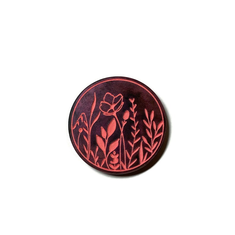 Pode incluir: Um descanso de copo circular de cor vermelho escuro com um desenho de flores e folhas cor-de-rosa.