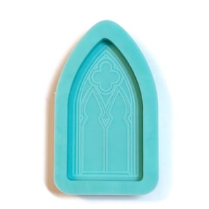 Puede incluir: Un molde de silicona turquesa para hacer manualidades de resina. El molde tiene forma de ventana de arco apuntado con un diseño decorativo en el interior.