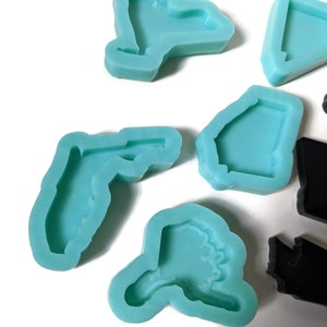 May include: A set of silicone molds in the shape of different states. The molds are light blue and are arranged on a white surface.