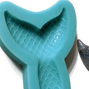 May include: A teal blue silicone mold shaped like a mermaid tail with a detailed scale pattern.