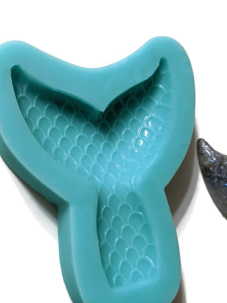 May include: A teal blue silicone mold shaped like a mermaid tail with a detailed scale pattern.