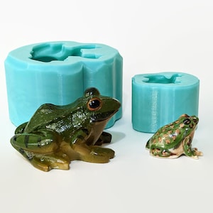 May include: Two silicone molds for making frog figurines. The larger mold is teal blue and has a detailed frog shape. The smaller mold is teal blue and has a simpler frog shape.