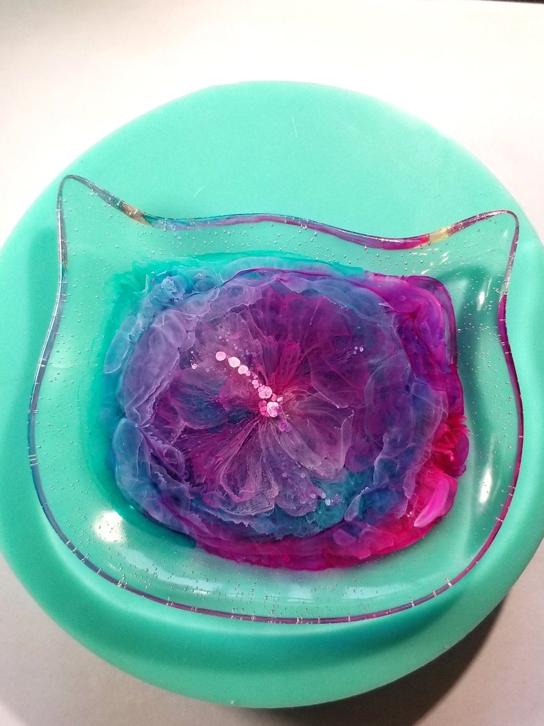 May include: A teal resin tray with a clear, raised edge. The tray features a pink, purple, and blue abstract design with white dots.