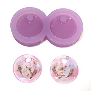 May include: A light purple silicone mold for making round pendants, with two cavities. Below are two finished pendants, each with a clear resin base and dried flowers, showcasing a floral design.
