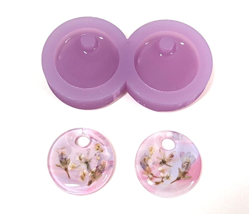 May include: A light purple silicone mold for making round pendants, with two cavities. Below are two finished pendants, each with a clear resin base and dried flowers, showcasing a floral design.