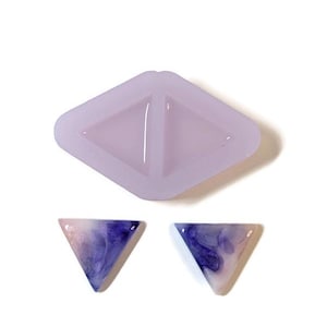 Puede incluir: Un molde de silicona para hacer pendientes de resina en forma de triángulo. El molde es de color morado claro y tiene dos cavidades en forma de triángulo. Se muestran dos pendientes de resina terminados, uno a cada lado del molde. Los pendientes son de color rosa claro y morado con un efecto marmoleado.