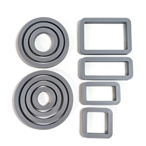 Könnte beinhalten: Graue Silikonformen in verschiedenen Formen. Zwei kreisförmige Formen mit konzentrischen Ringen und vier rechteckige und quadratische Formen. Alle Formen sind grau und befinden sich auf weißem Hintergrund.