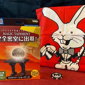 May include: A magic trick set with a box featuring the text "MAGIC TAINMENT" and Japanese text. A red cloth with a cartoon rabbit holding a wand is next to the box. A poker chip with the text "MORIS" is also visible.