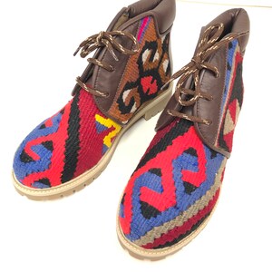 May include: A pair of brown leather ankle boots with colorful woven fabric panels. The fabric features a geometric pattern in shades of red, blue, yellow, and black.