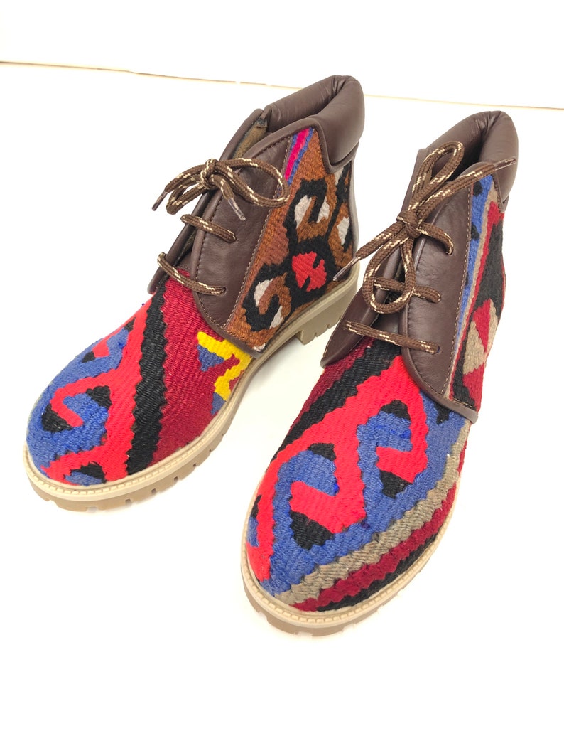 May include: A pair of brown leather ankle boots with colorful woven fabric panels. The fabric features a geometric pattern in shades of red, blue, yellow, and black.