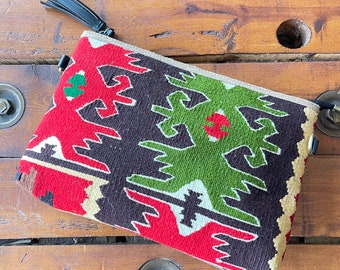 May include: A small, colorful clutch bag with a geometric pattern in shades of red, green, black, and white. The bag has a tassel and a zipper closure.