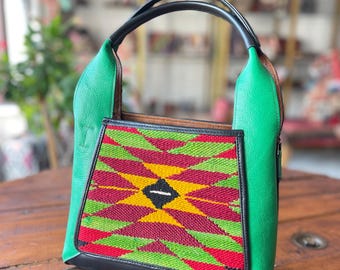 May include: A green leather tote bag with a black handle and a colorful geometric pattern on the front. The pattern is red, yellow, and green.