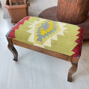 May include: A wooden footstool with a green, red, and yellow patterned cushion. The cushion has a geometric design.
