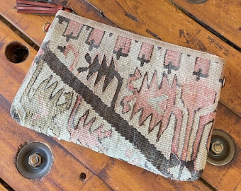 May include: A beige clutch purse with a brown leather tassel and a geometric pattern in shades of brown, pink, and white.