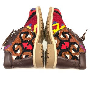 May include: A pair of brown leather ankle boots with colorful patterned fabric uppers. The fabric features a geometric design in shades of red, blue, yellow, and white.