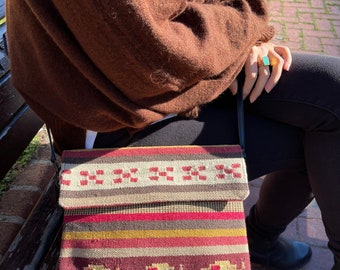 May include: A brown and beige striped crossbody bag with a flap closure. The bag has a woven pattern with red, yellow, and brown accents.