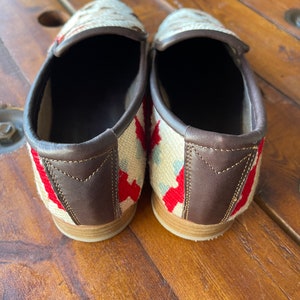 K&ouml;nnte beinhalten: Ein Paar wei&szlig;e, rote und blaue Slip-on-Schuhe mit braunen Lederbes&auml;tzen.