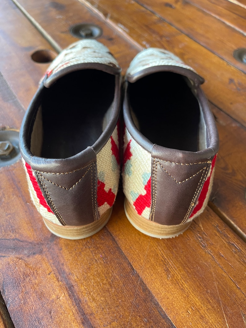 K&ouml;nnte beinhalten: Ein Paar wei&szlig;e, rote und blaue Slip-on-Schuhe mit braunen Lederbes&auml;tzen.