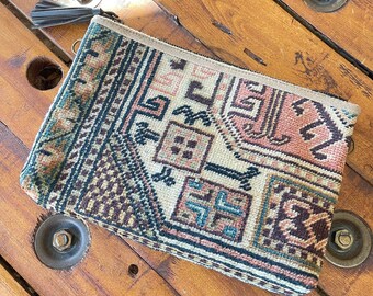 May include: A small, rectangular clutch purse with a beige background and a colorful geometric pattern. The purse has a zipper closure and a brown tassel.