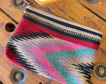 May include: A small, colorful woven clutch bag with a fringe tassel. The bag has a geometric pattern in shades of red, black, green, and brown.