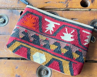 May include: A small red, black, and gold patterned zippered pouch with a black tassel. The pouch is made of woven fabric and has a geometric design.