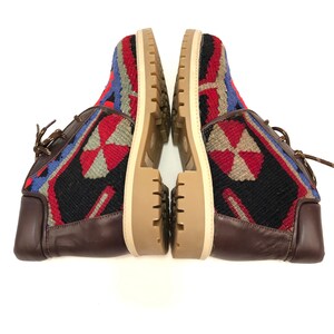 May include: A pair of brown leather ankle boots with a colorful woven pattern on the upper. The boots have a lace-up closure and a thick, cream-colored sole.
