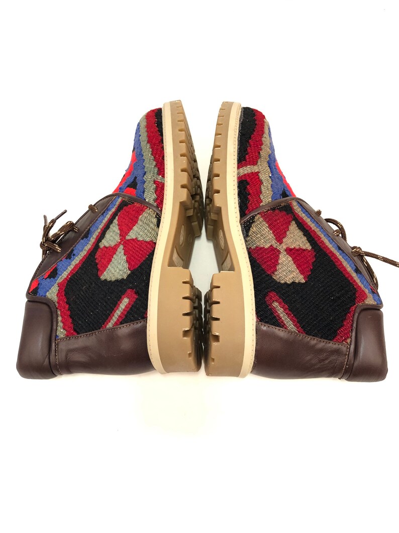 May include: A pair of brown leather ankle boots with a colorful woven pattern on the upper. The boots have a lace-up closure and a thick, cream-colored sole.