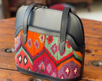 May include: A black leather handbag with a colorful woven pattern on the front. The bag has two top handles and a zipper closure.