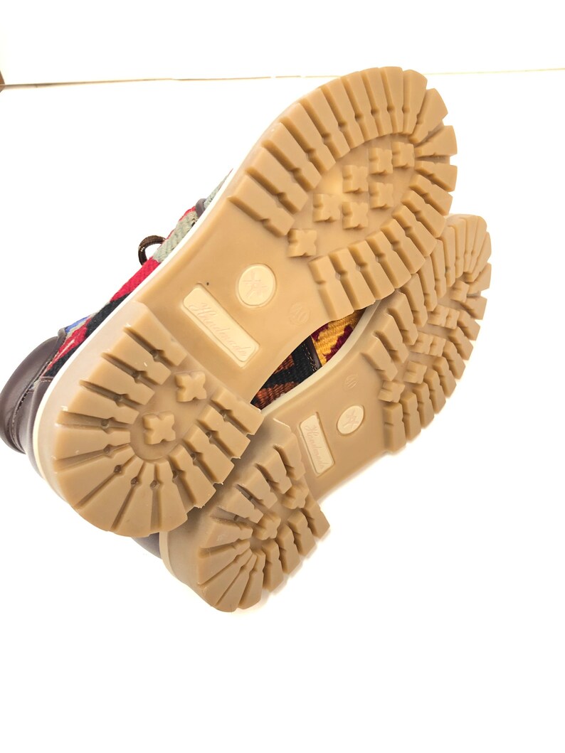 May include: Close-up of the bottom of a pair of brown leather shoes with a colorful patterned fabric upper. The shoes have a brown rubber outsole with a tread pattern.