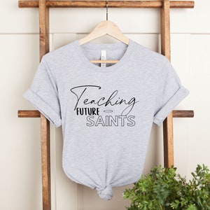 Teaching Future Saints Women's T-Shirt - Catholic Teacher's Gift - Catholic Homeschool Mom Tee - Catholic Homeschool Shirt Women's Clothing